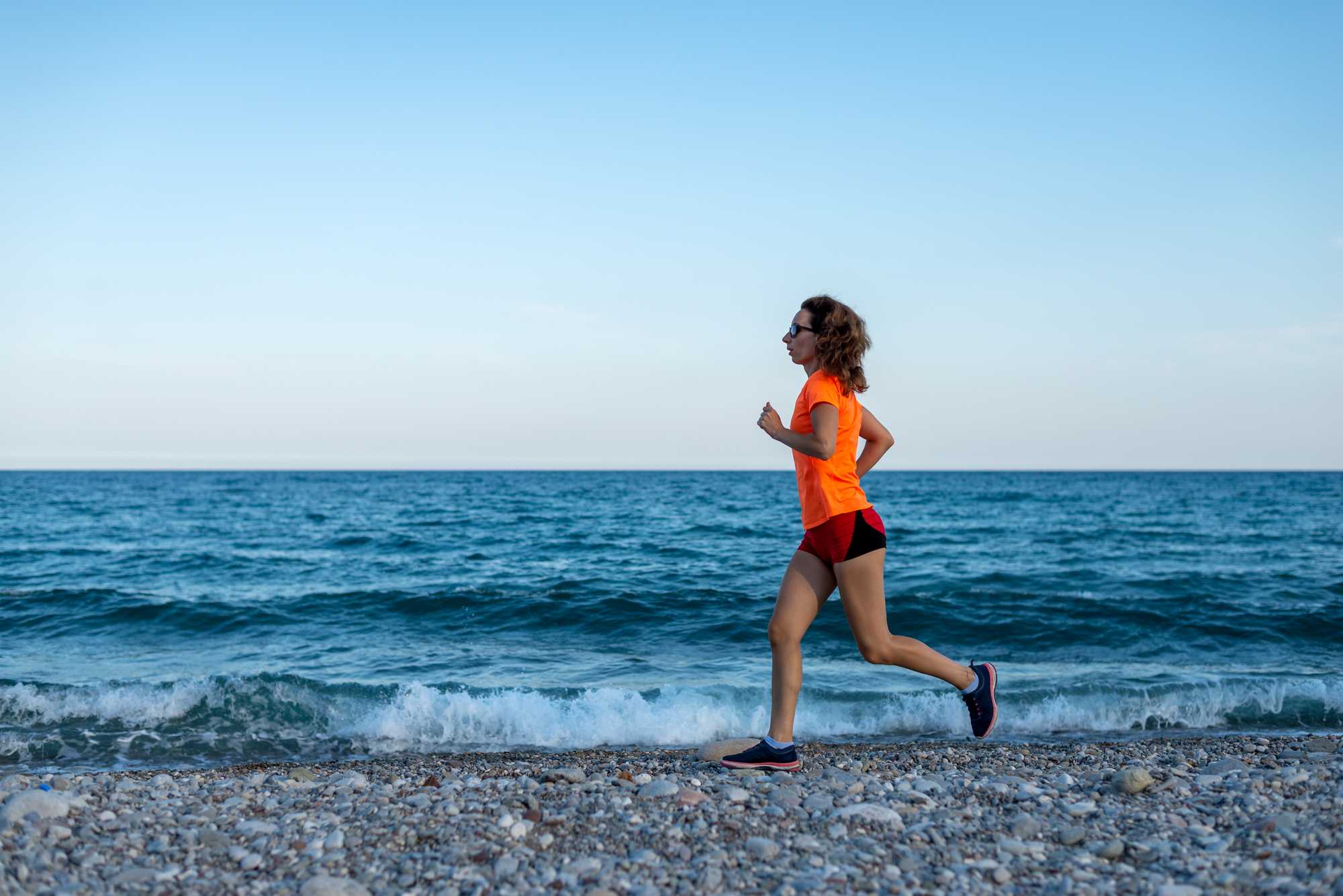 Woman running along a beach, against a blue sky