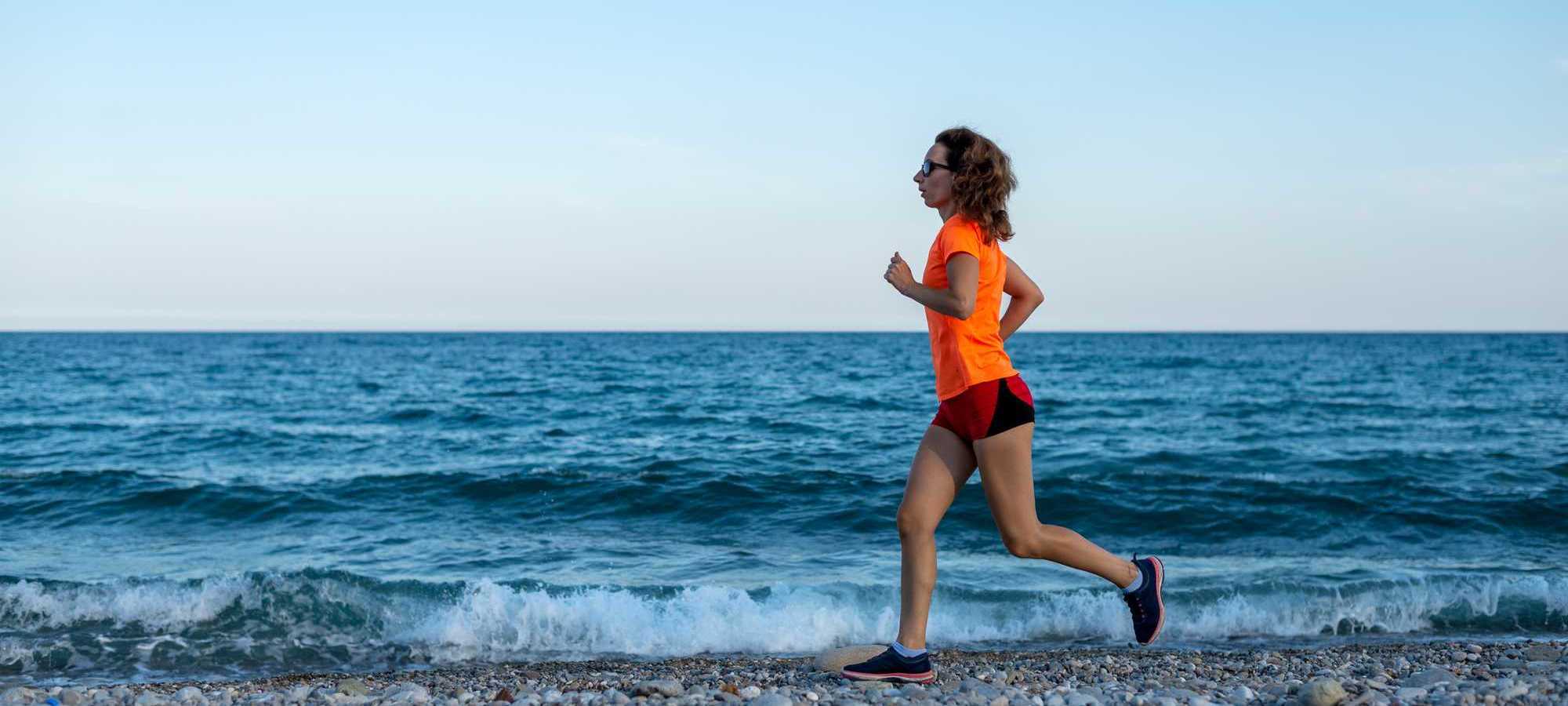 Woman running along a beach, against a blue sky